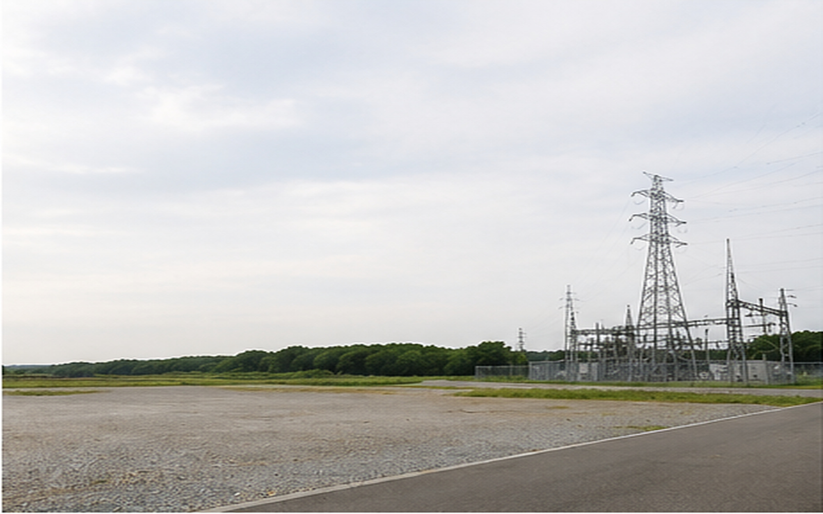 造成された平坦地の奥に送電鉄塔と変電設備が見える風景