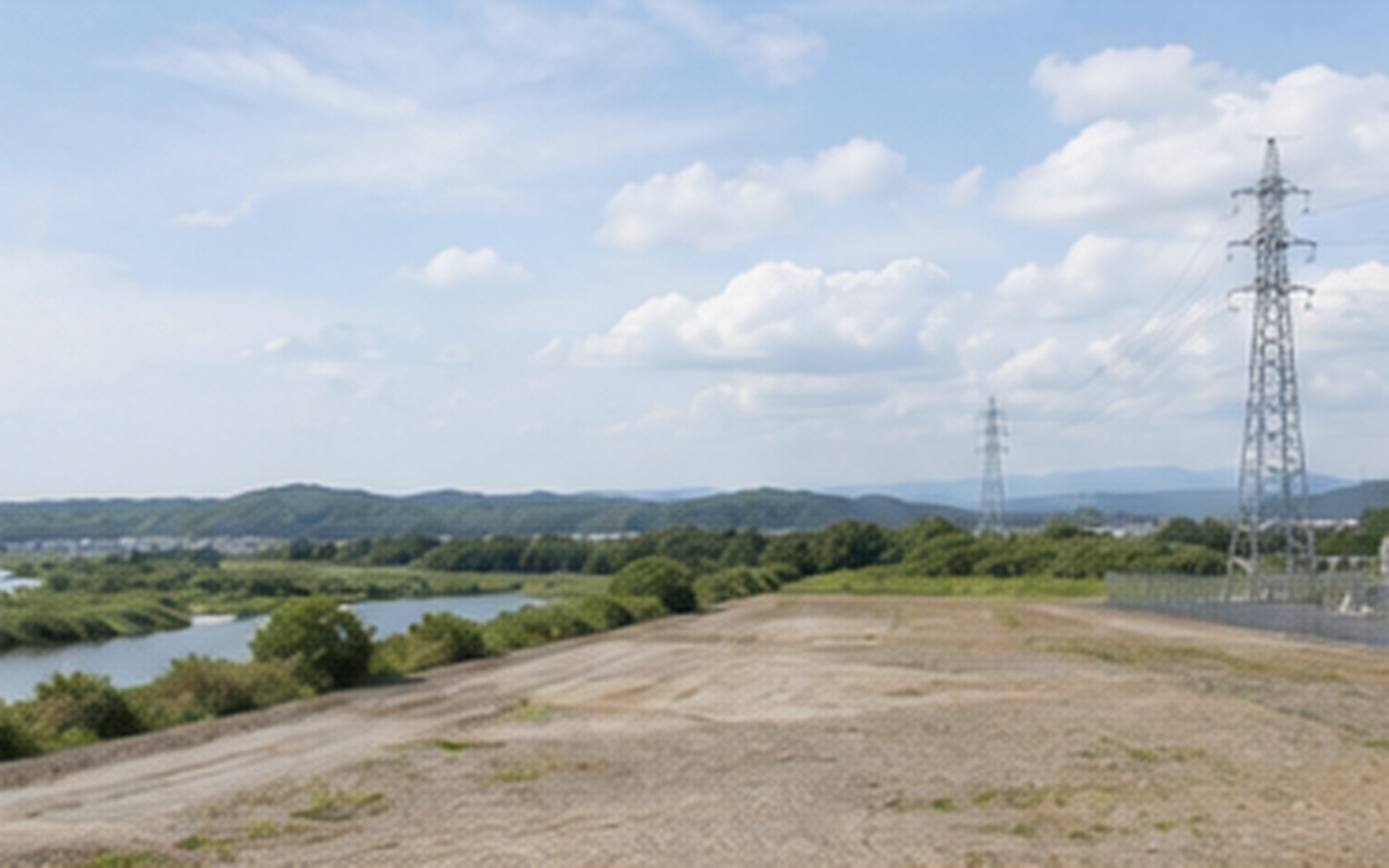 河川と丘陵に近い造成済みの蓄電池候補地を俯瞰する風景